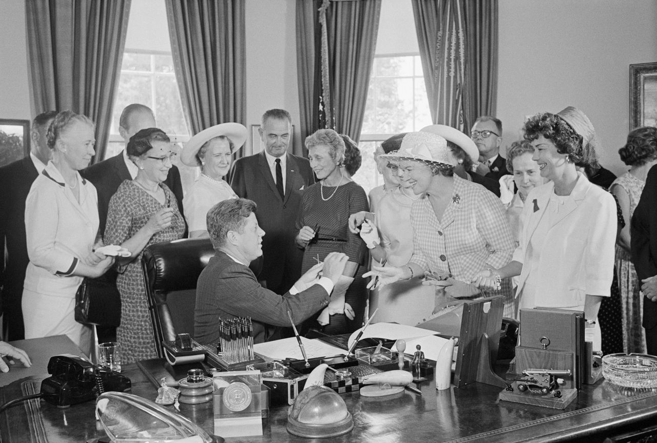 President John Kennedy hands out pens at the White House after signing the Equal Pay Act into law in 1963. The law mandates that men and women receive equal pay for equal work regardless of sex.
