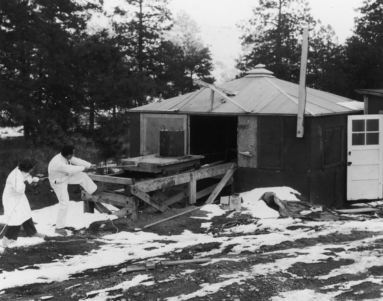 Scientists with the Manhattan Project manually haul a container of radioactive material from a shed in Los Alamos, New Mexico.