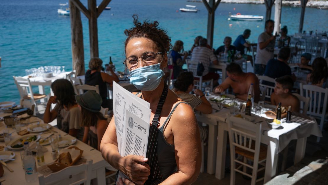 Waitress Vasiliki Besiou wears a face mask while waiting tables at the Takis Taverna in the pretty coastal village of Limeni.