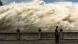 TOPSHOT - This photo taken on July 19, 2020 shows a security guard looking at his smartphone while water is released from the Three Gorges Dam, a gigantic hydropower project on the Yangtze river, to relieve flood pressure in Yichang, central China's Hubei province. - Rising waters across central and eastern China have left over 140 people dead or missing, and floods have affected almost 24 million since the start of July, according to the ministry of emergency management. (Photo by STR / AFP) / China OUT (Photo by STR/AFP via Getty Images)