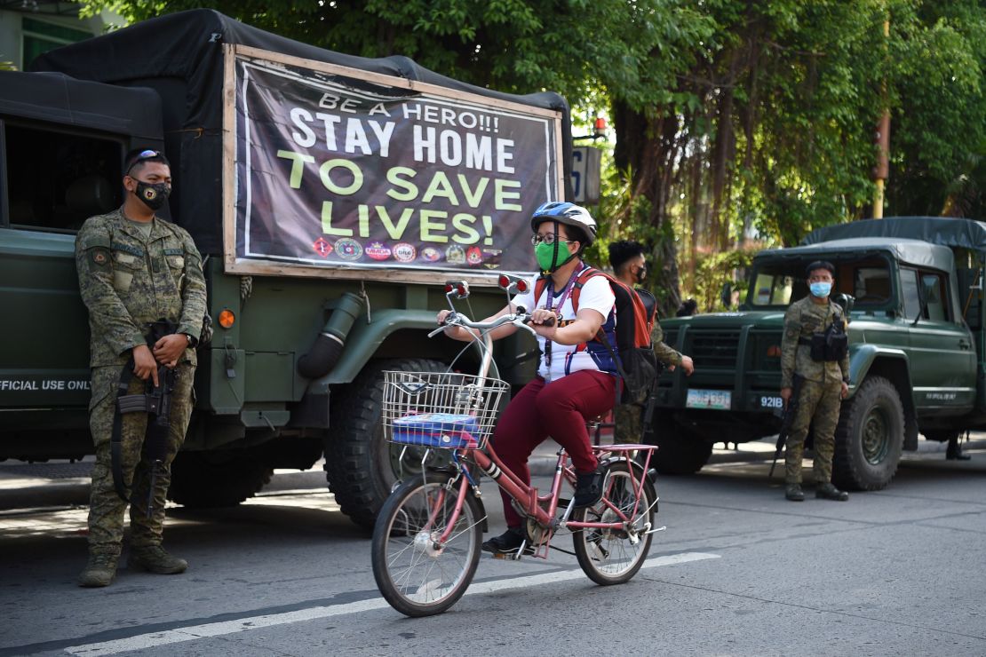 A resident rides her bicycle past armed soldiers along a street in Navotas in suburban Manila on July 16 after the local government reimposed a lockdown in the city due to increased COVID-19 infections.