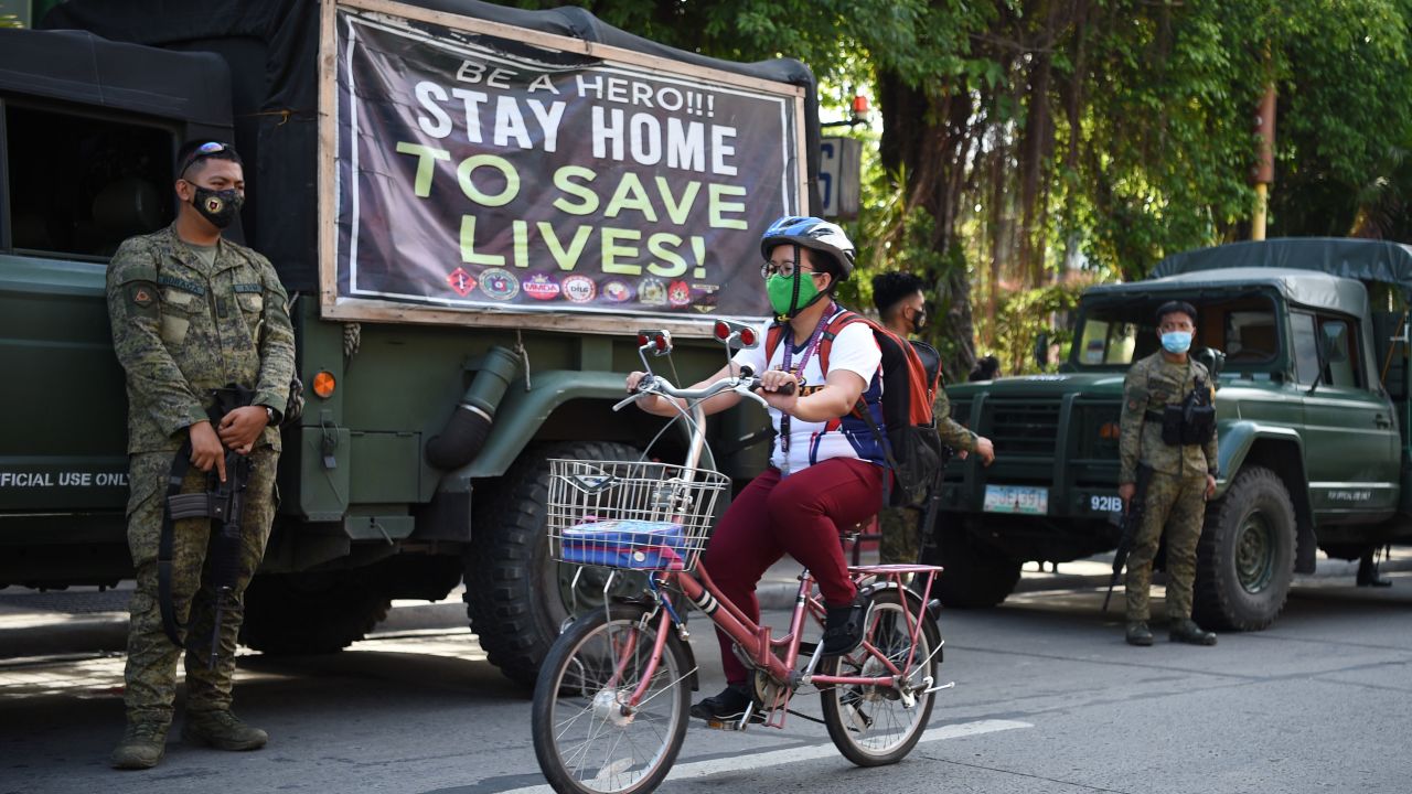 A resident rides her bicycle past armed soldiers along a street in Navotas in suburban Manila on July 16 after the local government reimposed a lockdown in the city due to increased COVID-19 infections.