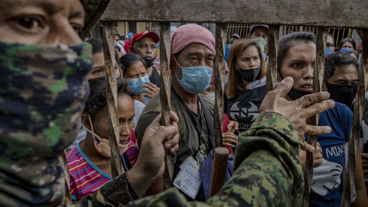 A police officer stands guard as  Filipinos out of work due to the coronavirus lockdown queue to receive government cash giveaways on May 11 in Rodriguez town, Rizal province, Philippines. 