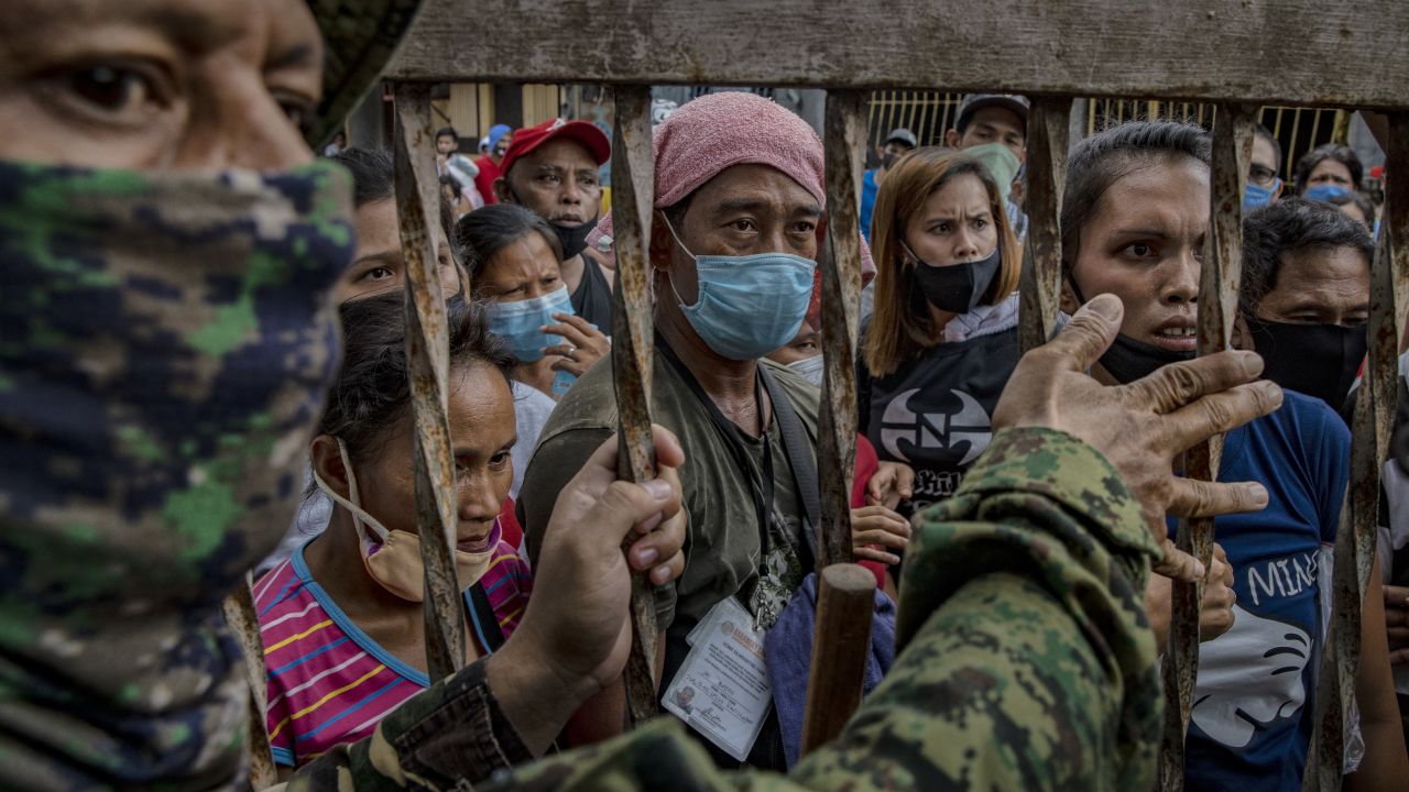 A police officer stands guard as Filipinos out of work due to the coronavirus lockdown queue to receive government cash giveaways on May 11 in Rodriguez town, Rizal province, Philippines.