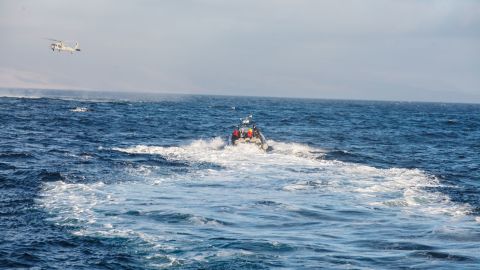 A US Navy MH-60 helicopter conducts aerial search and rescue while Sailors operate a rigid-hull inflatable boat during a search and rescue operation following the accident last July.