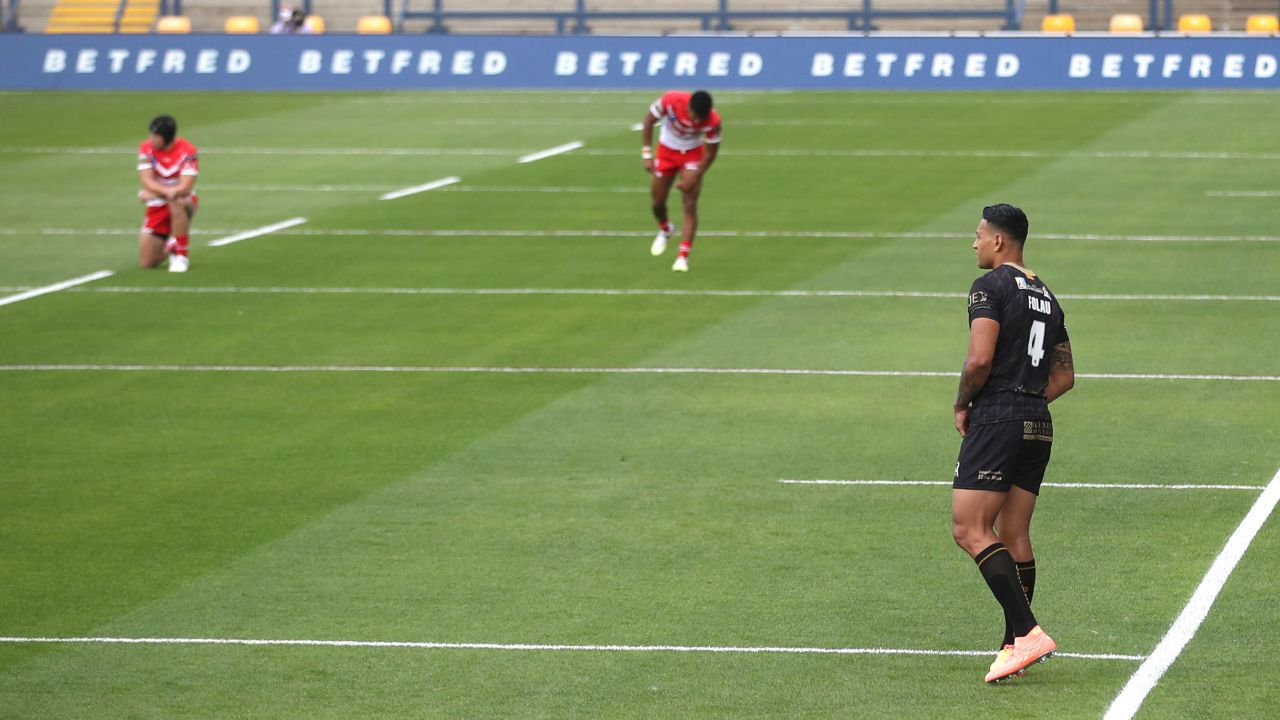 Catalans Dragons' Israel Folau remains standing as players kneel in support of the Black Lives Matter movement.