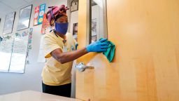 Amid concerns of the spread of COVID-19, Alma Odong wears a mask as she cleans a classroom at Wylie High School in Wylie, Texas. The cost of bringing students back to classrooms is proving a major stumbling block to safely reopening schools across the U.S. (AP Photo/LM Otero, File)