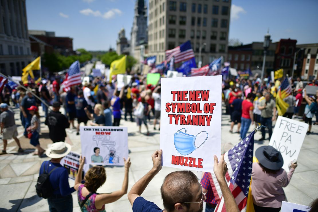 A demonstrator holds a sign with a face mask, calling it "THE NEW SYMBOL OF TYRANNY -- MUZZLE," outside the Pennsylvania Capitol Building in May.