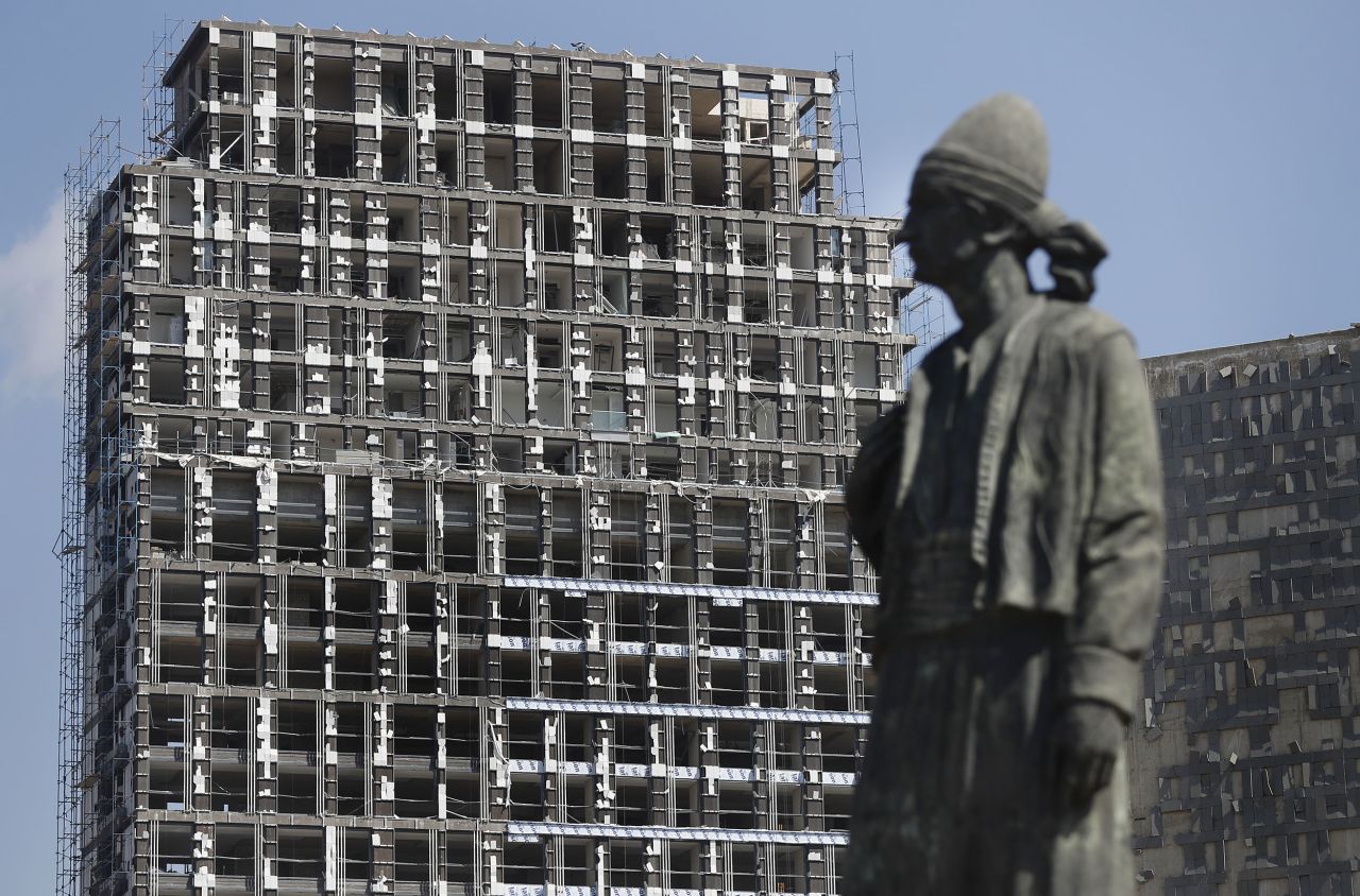 A statue representing the Lebanese expatriate is seen in front of a building that was damaged by the explosion.
