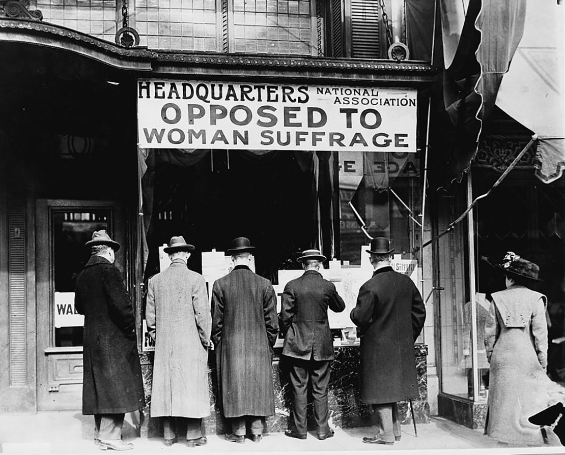 Photograph shows men looking at material posted in the window of the National Anti-Suffrage Association headquarters