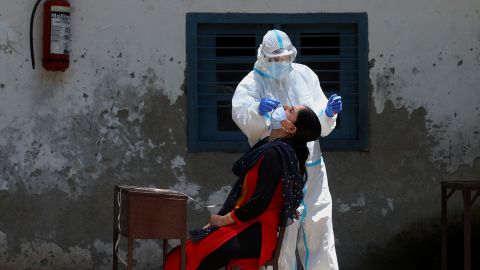 A medic wearing personal protective equipment collects a swab sample in India. 