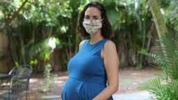 A pregnant woman wears a face mask while posing for a photo. 