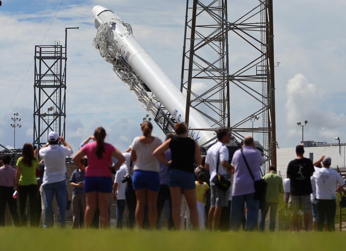 People watch as a SpaceX Falcon 9 rocket attached to the cargo-only Dragon capsule is prepared for a scheduled evening launch on October 7, 2012 in Cape Canaveral, Florida, to bring cargo of clothing, equipment and science experiments to the International Space Station.