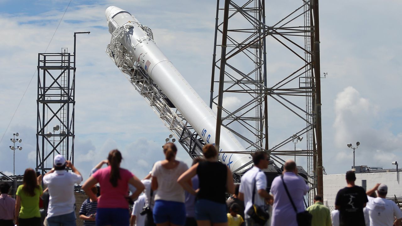 People watch as a SpaceX Falcon 9 rocket attached to the cargo-only Dragon capsule is prepared for a scheduled evening launch on October 7, 2012 in Cape Canaveral, Florida, to bring cargo of clothing, equipment and science experiments to the International Space Station.