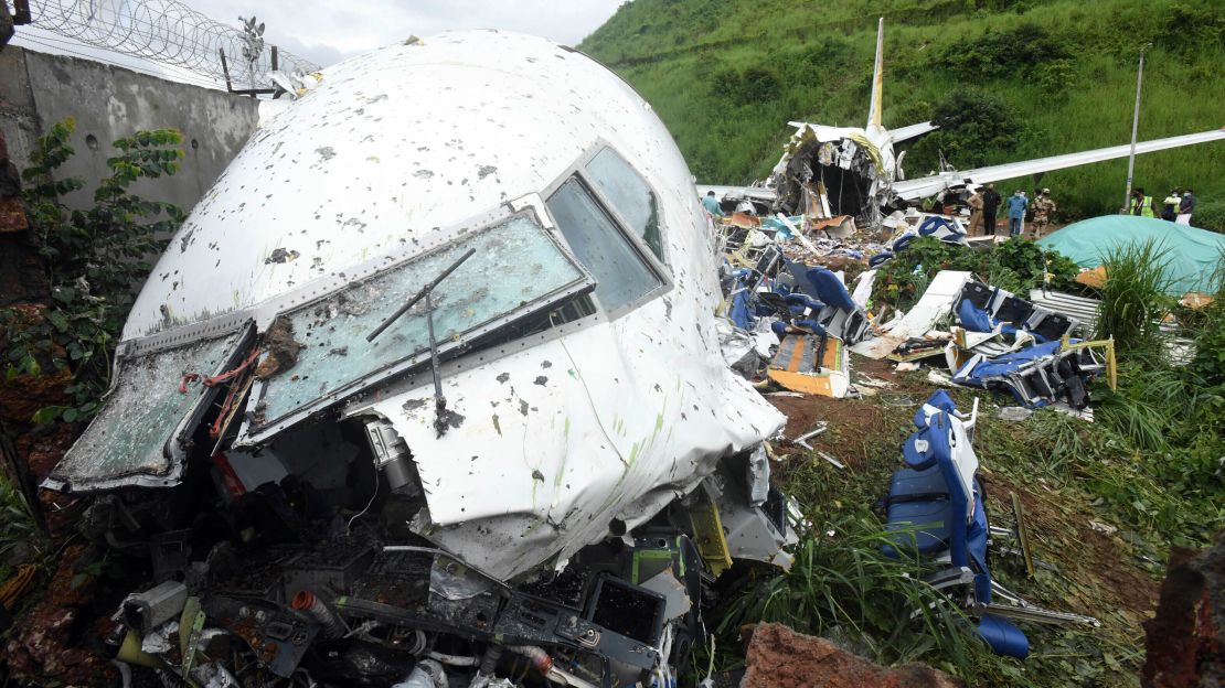 People stand Saturday by the debris of the Air India Express flight that skidded off a runway while landing in Kozhikode, Kerala state, India.