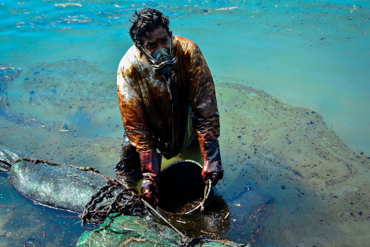 A man scoops leaked oil from the water.