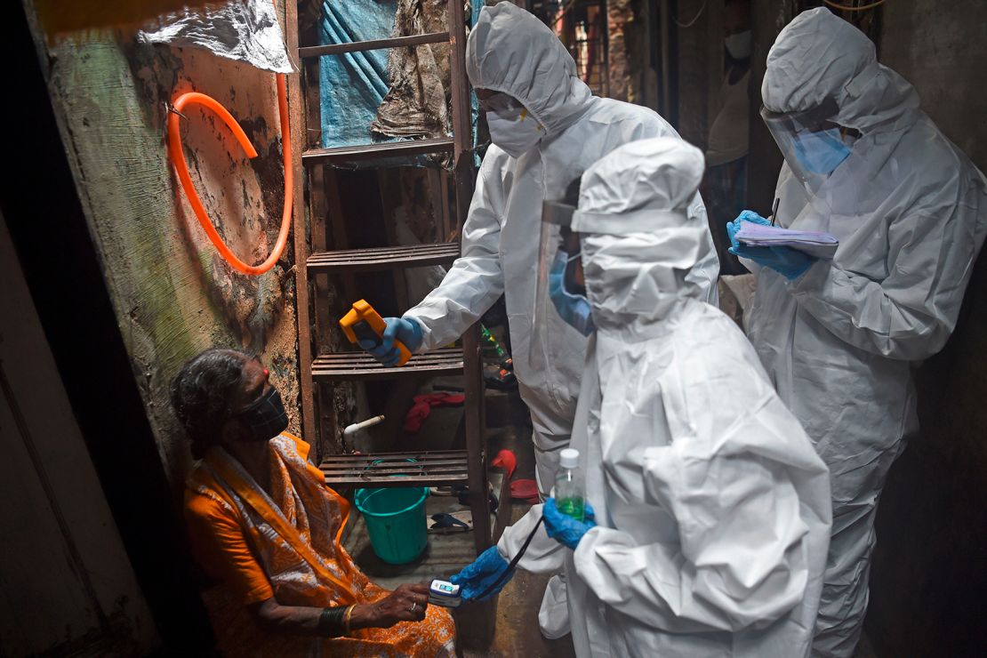 Medical volunteers wearing PPE gear take temperature reading of a woman as they conduct a door-to-door medical screening inside Dharavi slums in Mumbai on July 9, 2020.