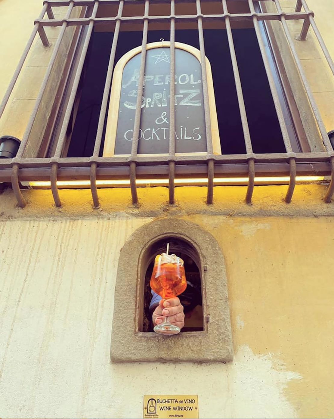 An Aperol spritz being served through a wine window at Osteria delle Brache