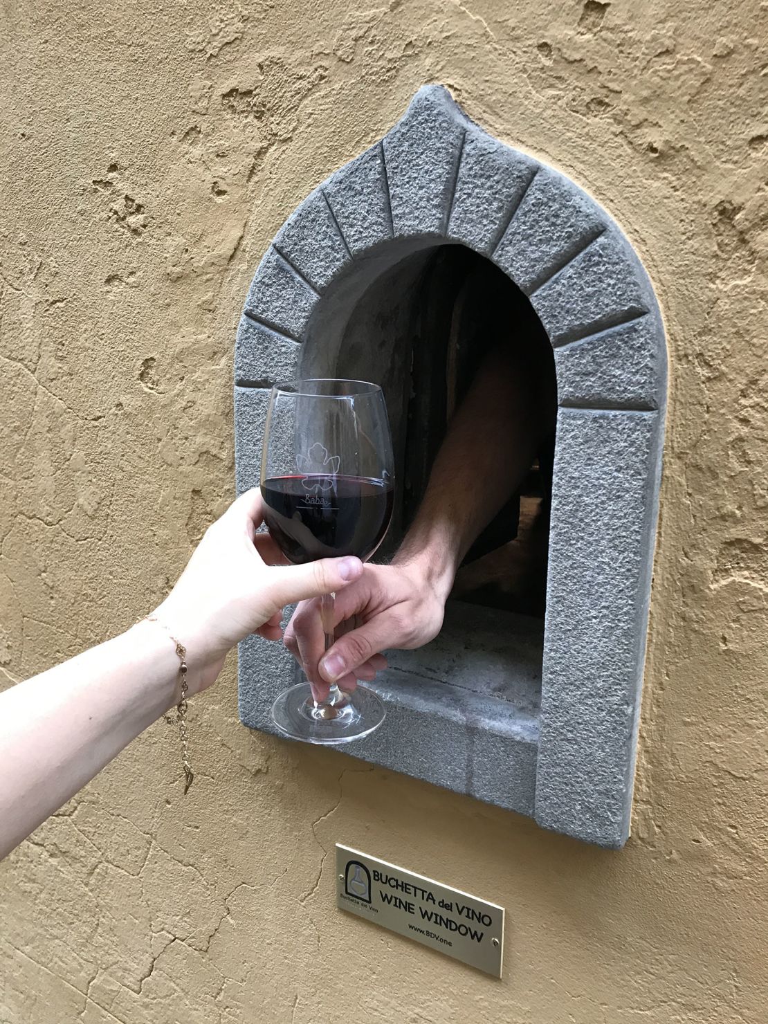 A glass of red being served through a wine window in Florence.  