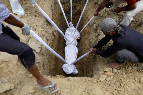 A coronavirus victim is lowered into the ground during her funeral in New Delhi on August 7.
