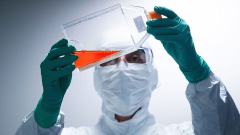 A lab technician wearing Personal Protective Equipment (PPE) looks at a bottle containing a reagent before performing vaccine tests at a French pharmaceutical company Sanofi's laboratory in Val de Reuil on July 10, 2020. (Photo by Joel Saget/AFP/Getty Images)