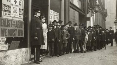 A line of people waiting for flu masksin 1918 in San Francisco. A sign on the window bearing the Red Cross logo reads: "Influenza. Wear Your Mask."