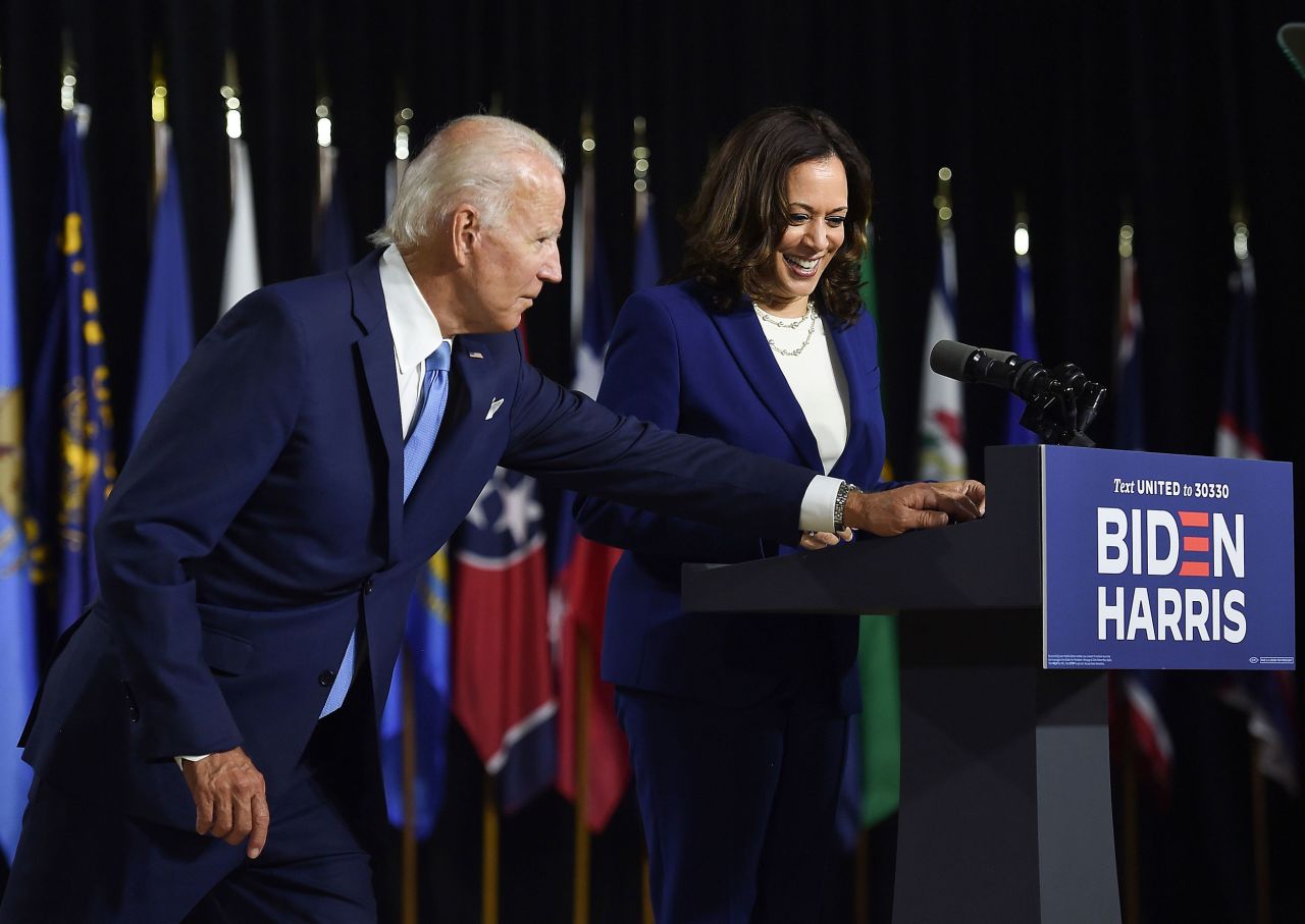 Biden reaches over to grab his face mask before Harris delivered her speech on Wednesday.
