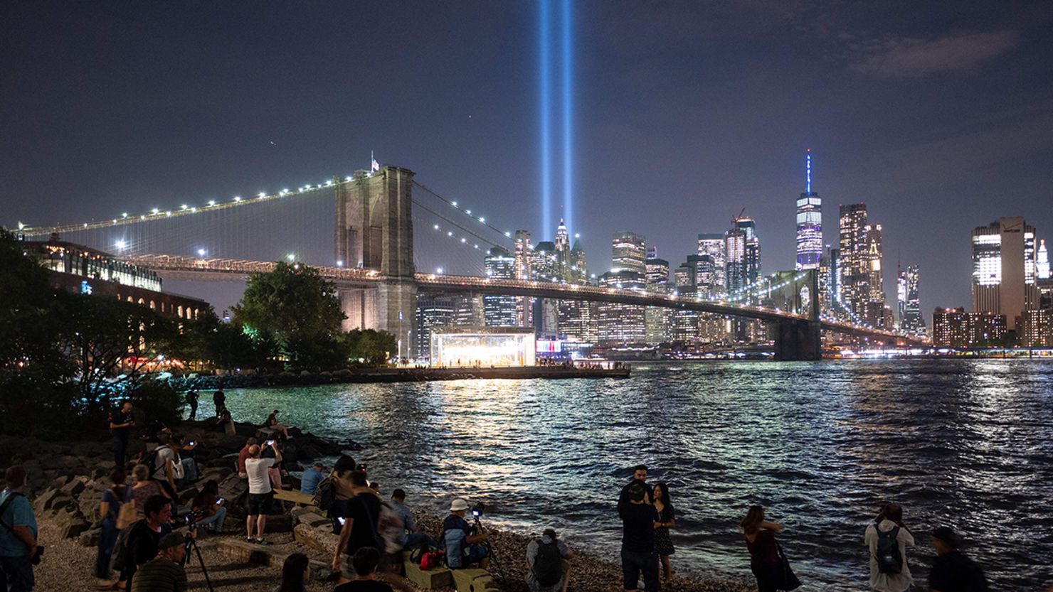 People on the shore watch the "Tribute in Light" shining into the New York sky on September 11, 2019.