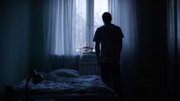 A man stands by a window in a dark room