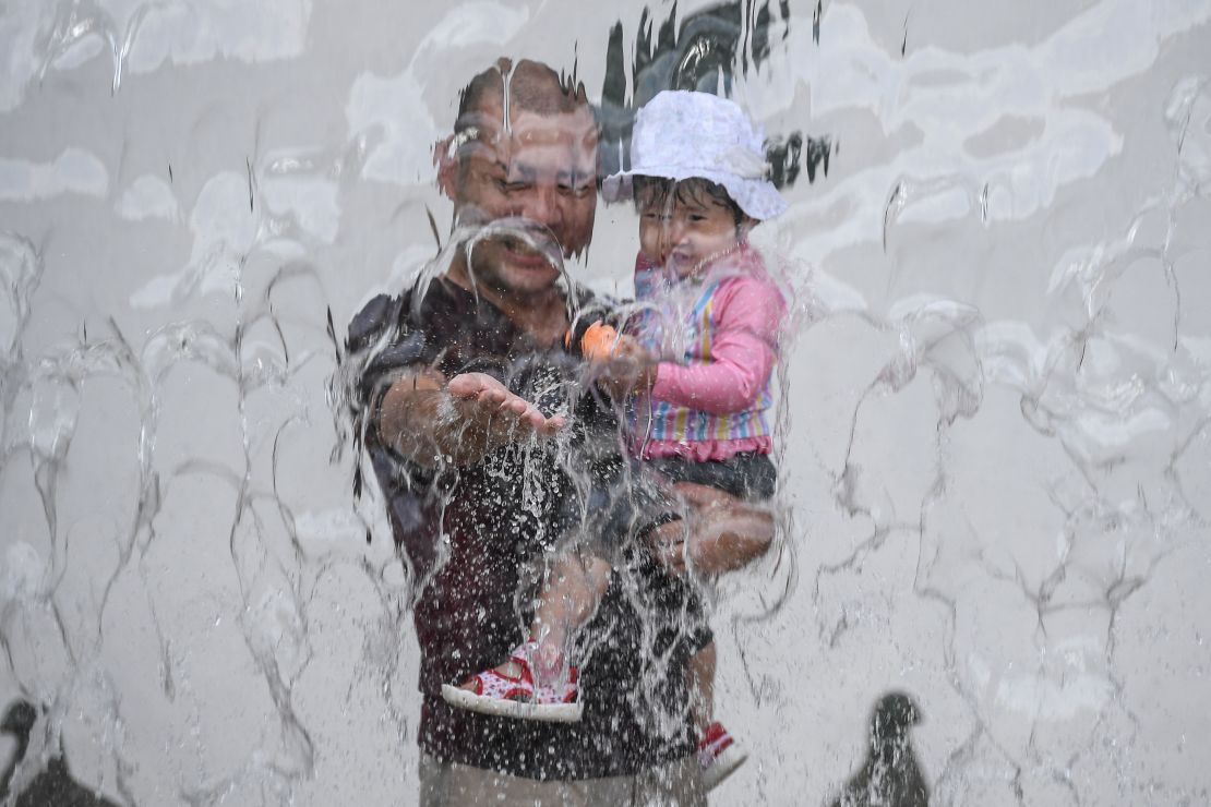 A father and his daughter play in a water fountain at a park during a heat wave in Tokyo on August 14, 2020. 