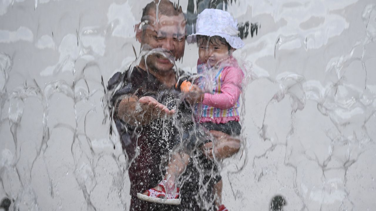 A father and his daughter play in a water fountain at a park during a heat wave in Tokyo on August 14, 2020.