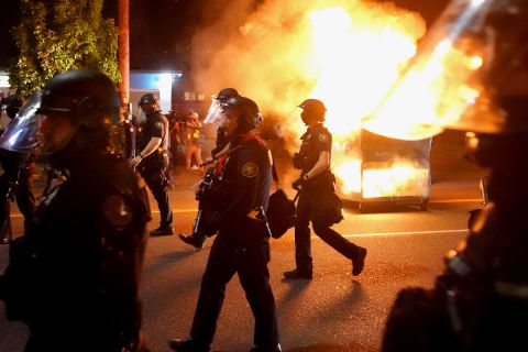 Portland police walk past a dumpster fire while dispersing a crowd of protesters on August 14.