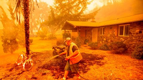A resident hoses down a burning bicycle and tree as the Hennessey Fire approaches a home in Napa, California. 