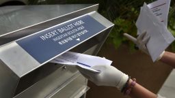 In this July 7, 2020 photo, a woman wearing gloves drops off a mail-in ballot at a drop box in Hackensack, New Jersey,