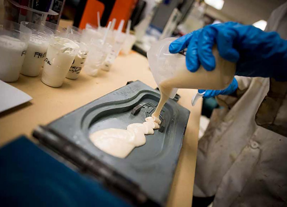 A student pours polyurethane into a flip flop mold.