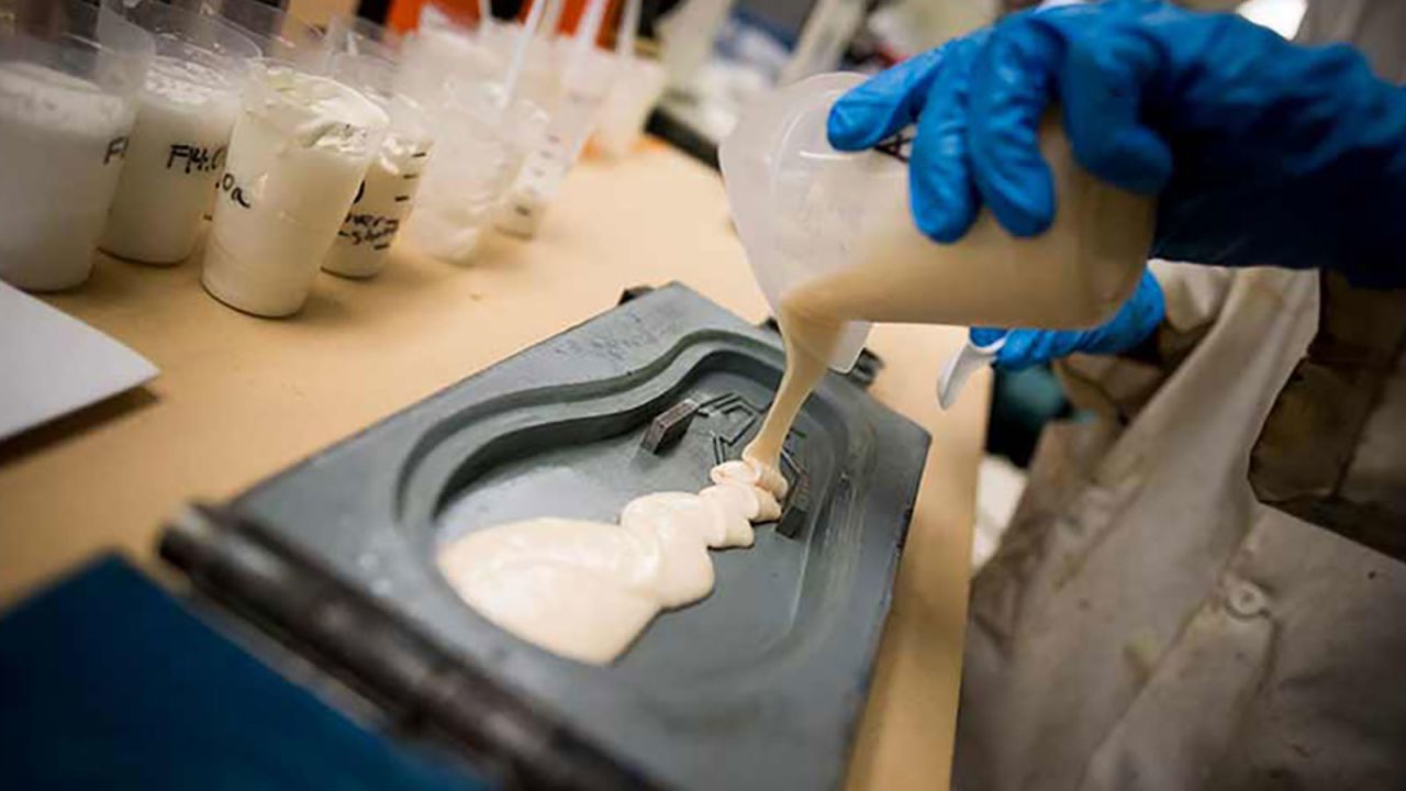 A student pours polyurethane into a flip flop mold.