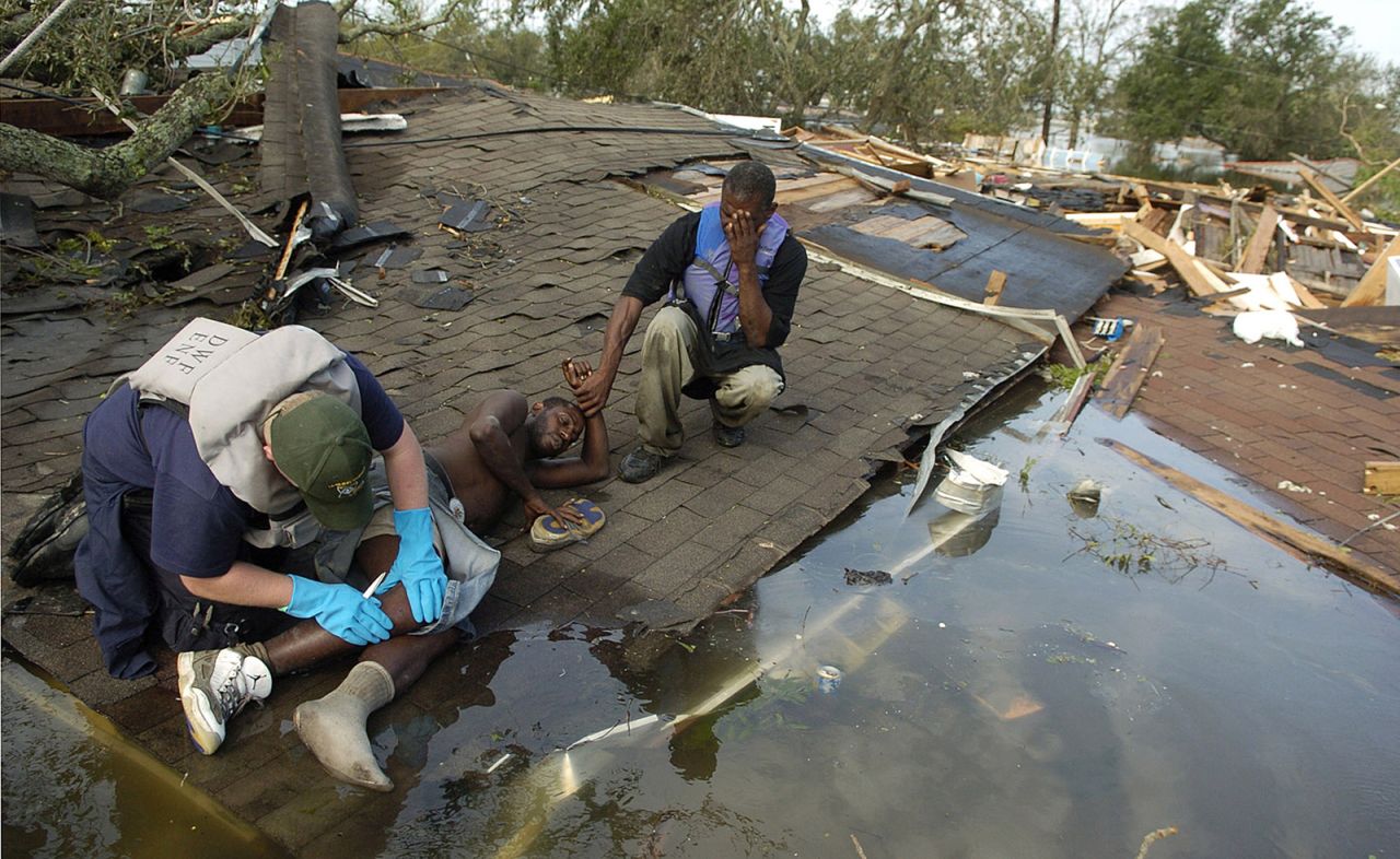Paramedic David Mitchell examines Greg Farteberry on the roof of a destroyed home in New Orleans as Farteberry's friend Eric Charles holds his hand. Farteberry broke his ankle during the storm and spent the night on the roof until he was rescued.