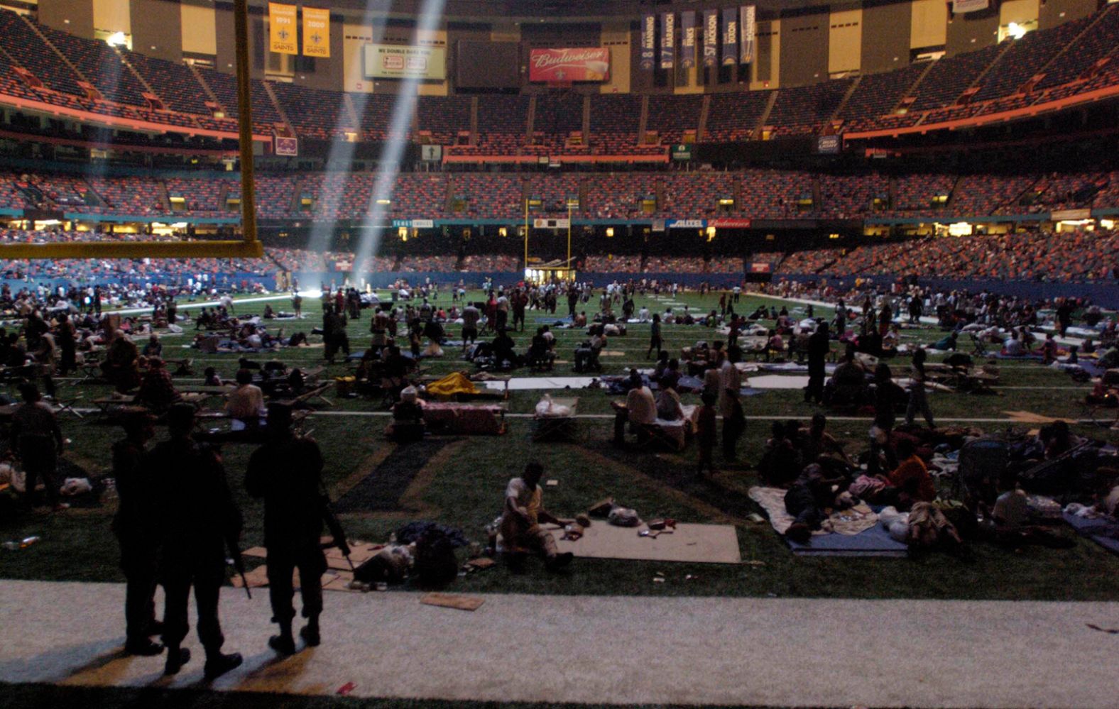 Members of the National Guard, standing in the foreground, watch over evacuees who took shelter at the Superdome in New Orleans. The shaft of light came from a hole in the roof of the dome.