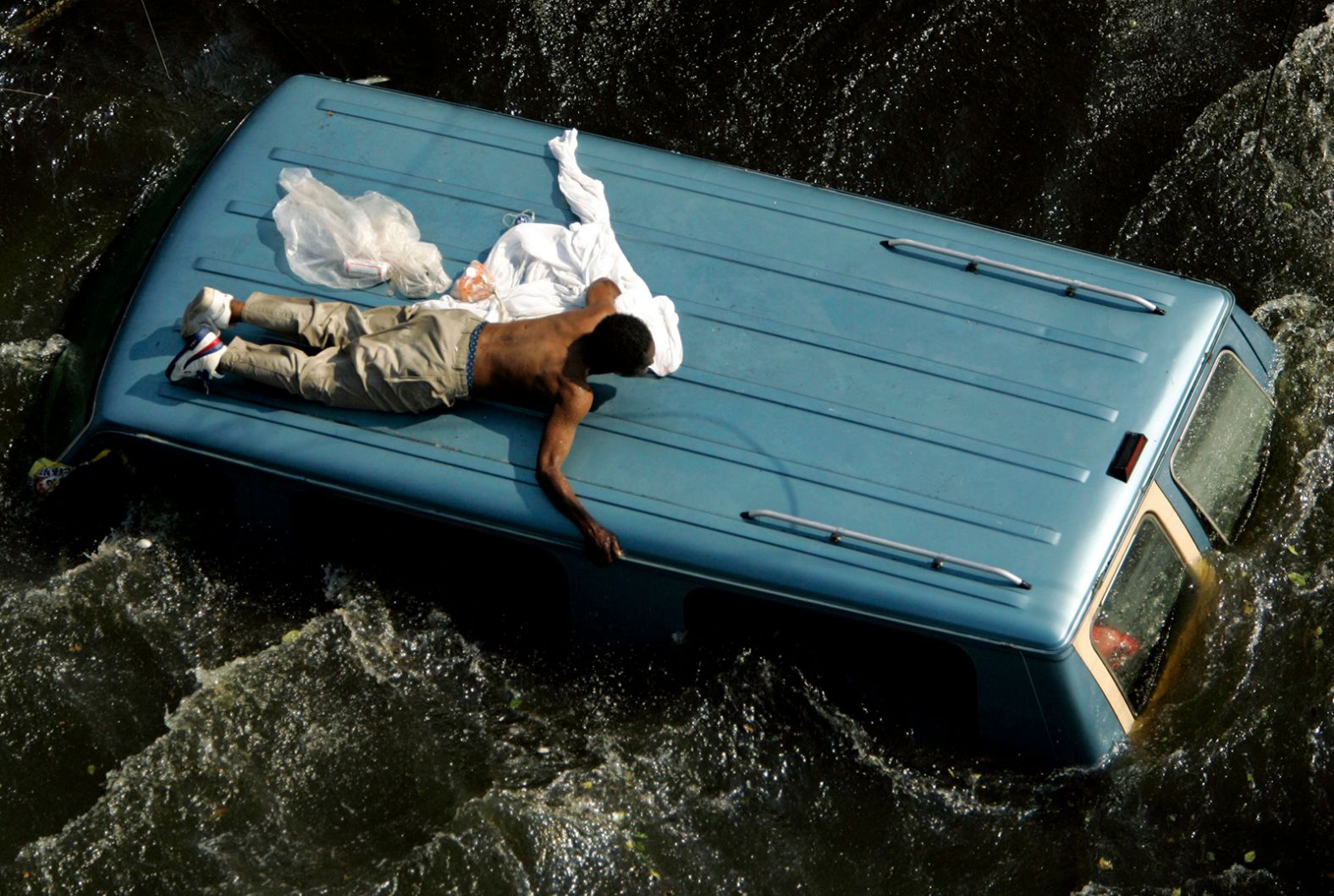 A man clings to the top of a vehicle in New Orleans before being rescued by the Coast Guard.