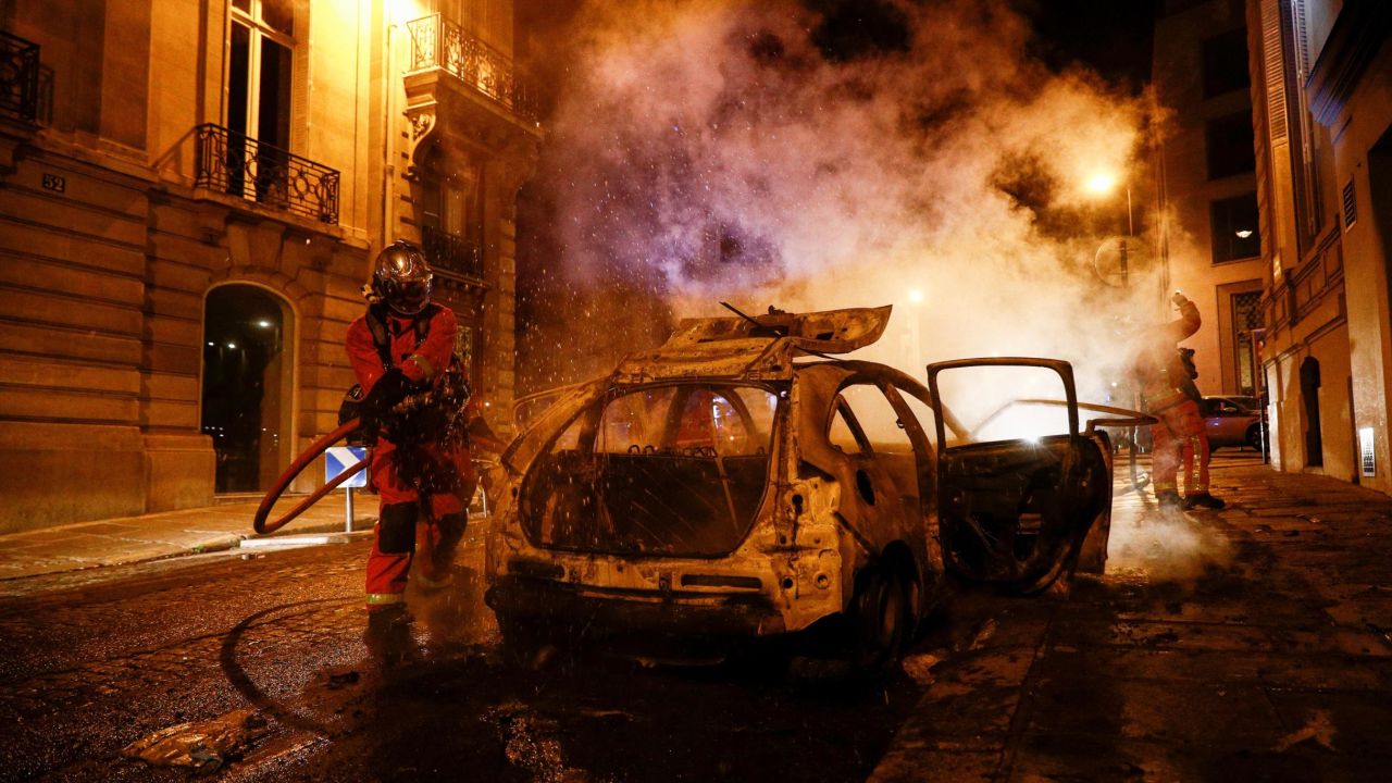 Firefighters extinguish a burning car near the Champs-Élysées following PSG's Champions League final defeat.