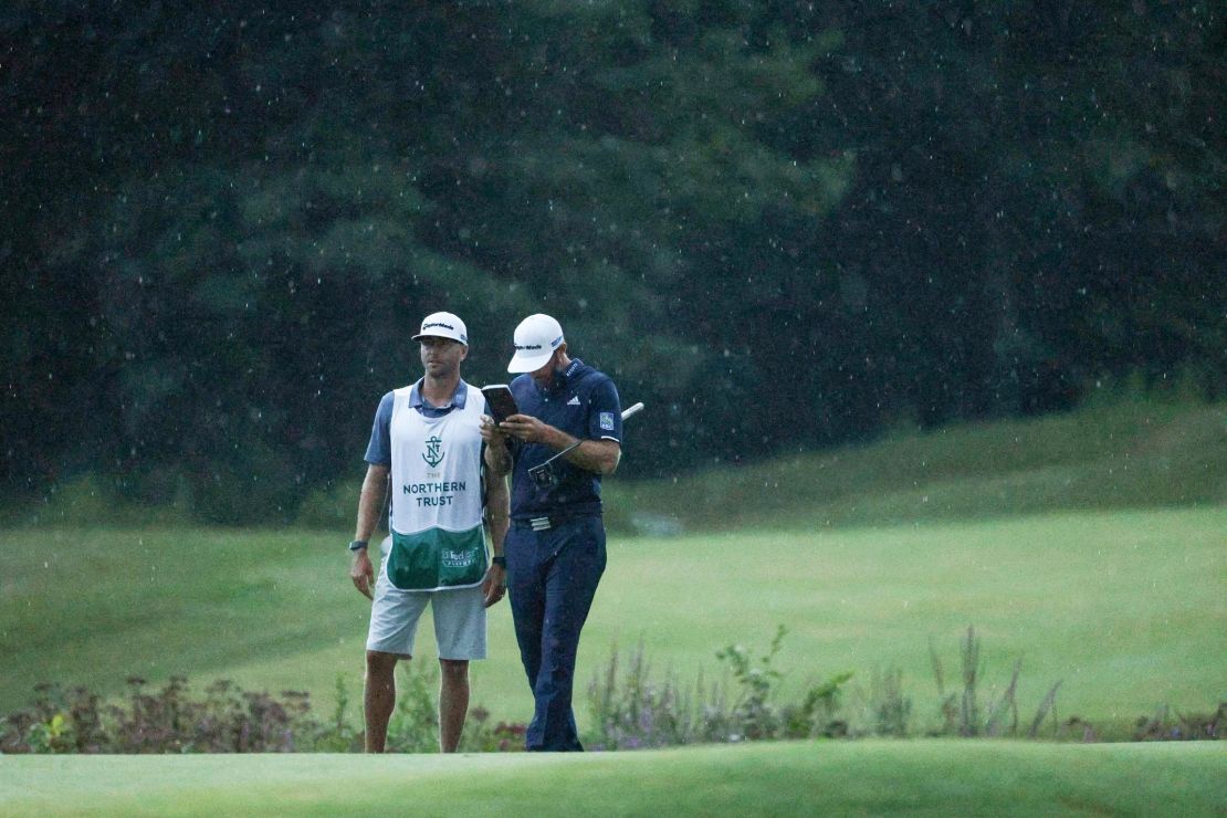 As the rain falls on them, Johnson lines up a putt with the help of  caddie Austin Johnson on the 18th green.