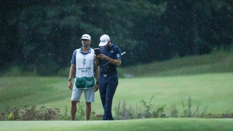 As the rain falls on them, Johnson lines up a putt with the help of caddie Austin Johnson on the 18th green.