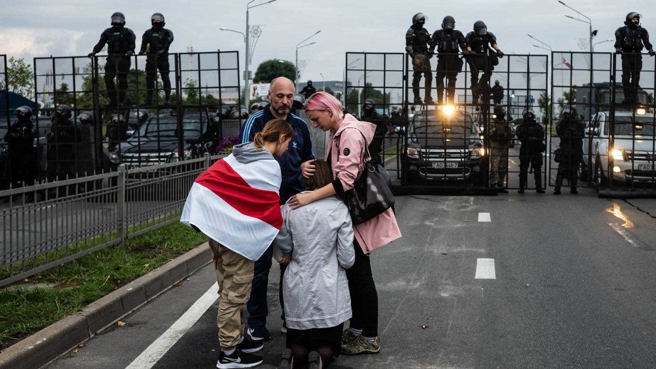 Anti-government protesters console a praying woman near riot police in Minsk on Sunday.