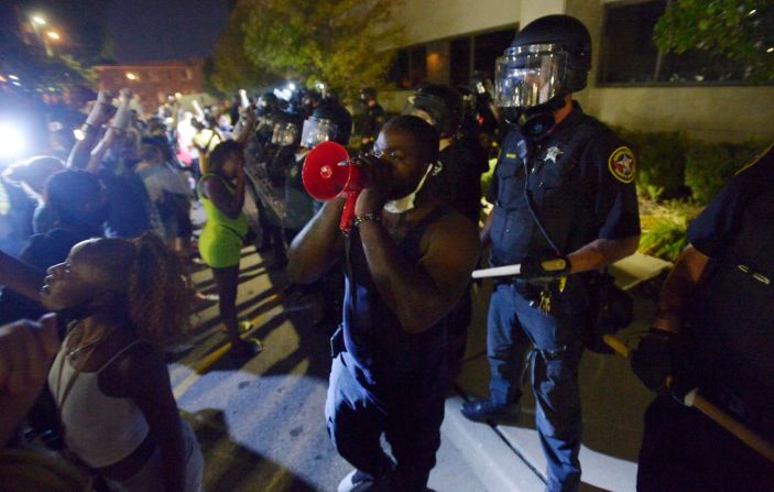 Demonstrators stand in front of a line of police at the Public Safety Building.