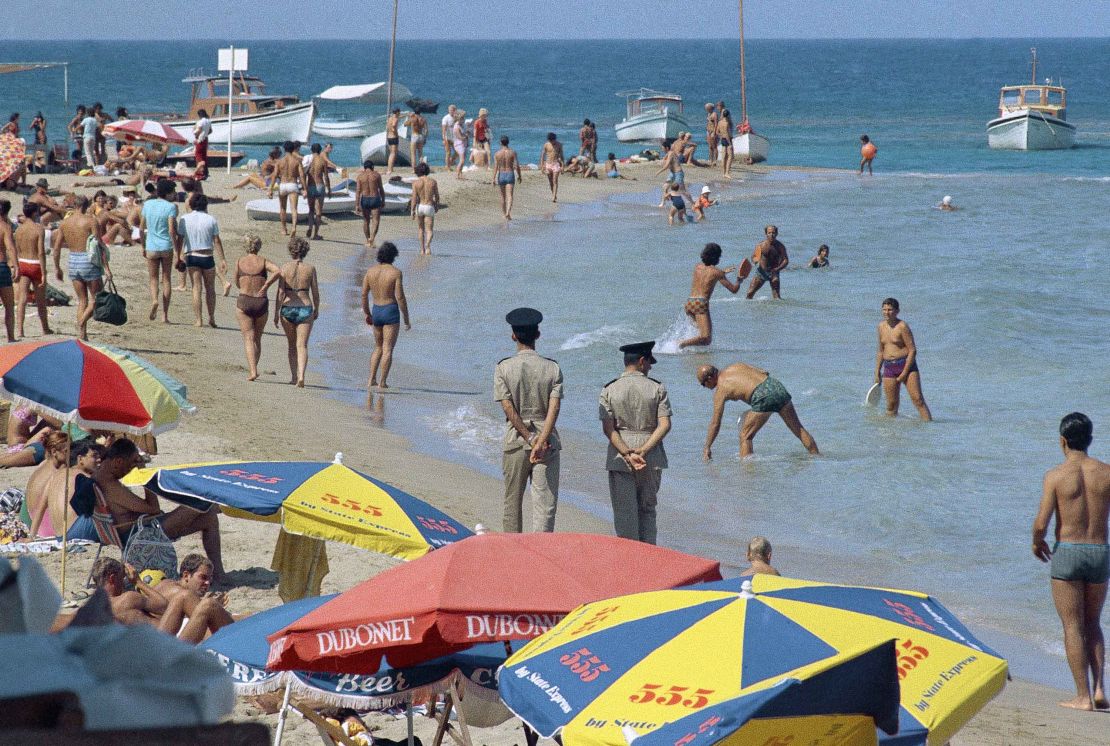 Famagusta beach filled with swimmers, sailors and police who walk the beach with hands behind them for security reasons, in 1970, Kyrenia, Cyprus.