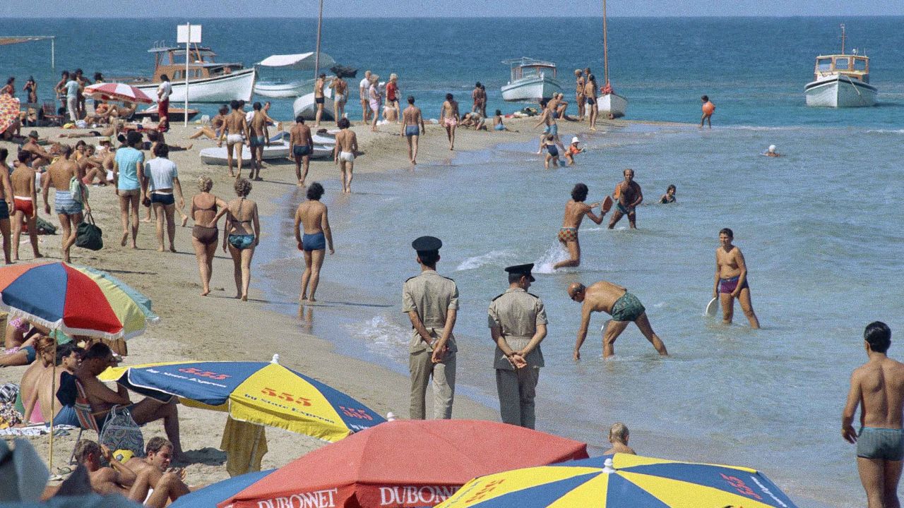 Famagusta beach filled with swimmers, sailors and police who walk the beach with hands behind them for security reasons, in 1970, Kyrenia, Cyprus.