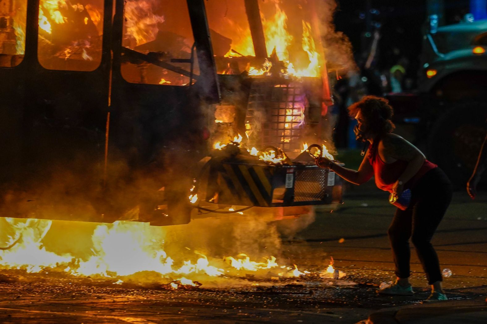 A protester lights a cigarette on a garbage truck that was set on fire during protests.