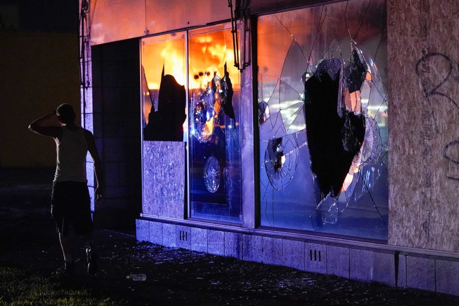 Burning structures are reflected in a building's broken glass as a protester walks past on August 24.