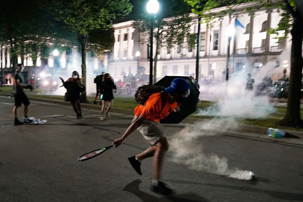 A demonstrator uses a tennis racket to return a tear-gas canister toward police lines.