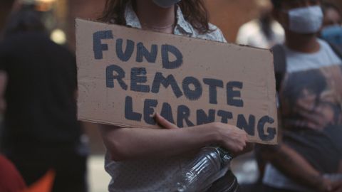 A teacher holds a sign reading "fund remote learning" at a protest on August 20, 2020.